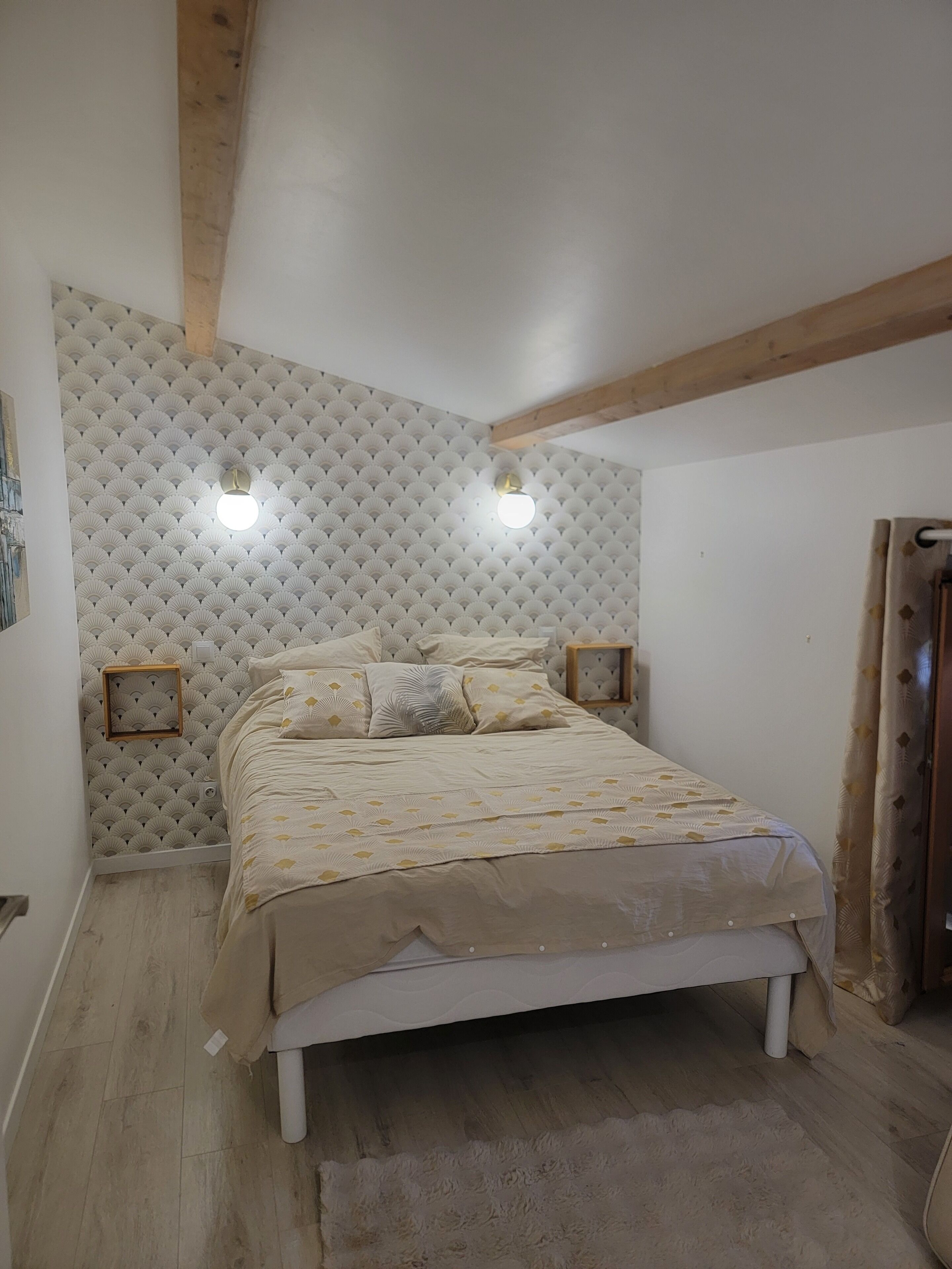 A bedroom with a bed, a headboard with a fan pattern, two bedside lamps, and a wooden ceiling beam.