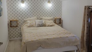 Een slaapkamer met een bed, een hoofdbord met een ventilatorpatroon, twee nachtlampjes en een houten balk in het plafond.