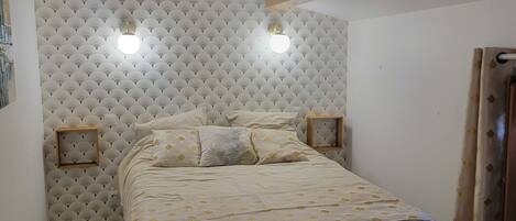 A bedroom with a bed, a headboard with a fan pattern, two bedside lamps, and a wooden ceiling beam.