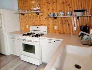 A kitchen with a stove, oven, and dishwasher, wooden paneling, and a sink.