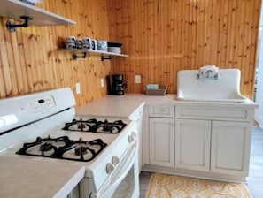 Una cocina con estufa a gas, armarios blancos, cafetera y lavamanos.