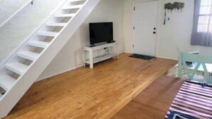 Ein Zimmer mit Holzboden, einer weißen Treppe, einem Fernseher auf einem weißen Beistelltisch und einer Tür mit Fußmatte.