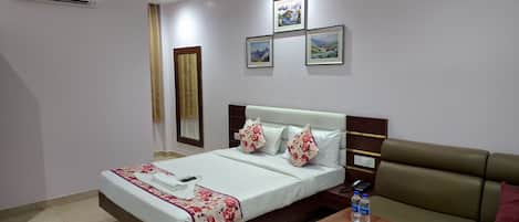 A hotel room with a bed, a bedside table with a book, a sofa, a ceiling fan, and framed pictures on the wall.