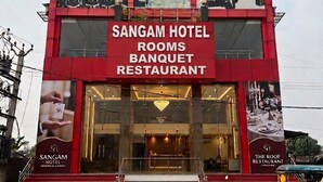 Un hôtel à la façade rouge, avec une enseigne indiquant « SANGAM HOTEL » et « THE ROOF RESTAURANT ».