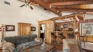 Una sala de estar acogedora con techo de madera, un sofá, una mesa de centro y una zona de bar con taburetes.