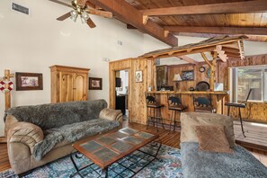 Ein gemütliches Wohnzimmer mit Holzbalkendecke, einer Couch, einem Couchtisch und einer Bar mit Hockern.