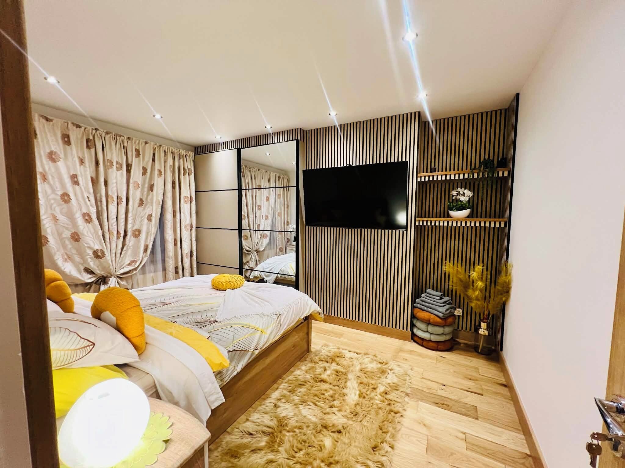 Un dormitorio con cama, cortinas, televisor, espejo y suelo de madera.