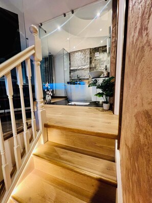 Un escalier menant à une salle de bain équipée d’une baignoire, d’un lavabo et d’un miroir.