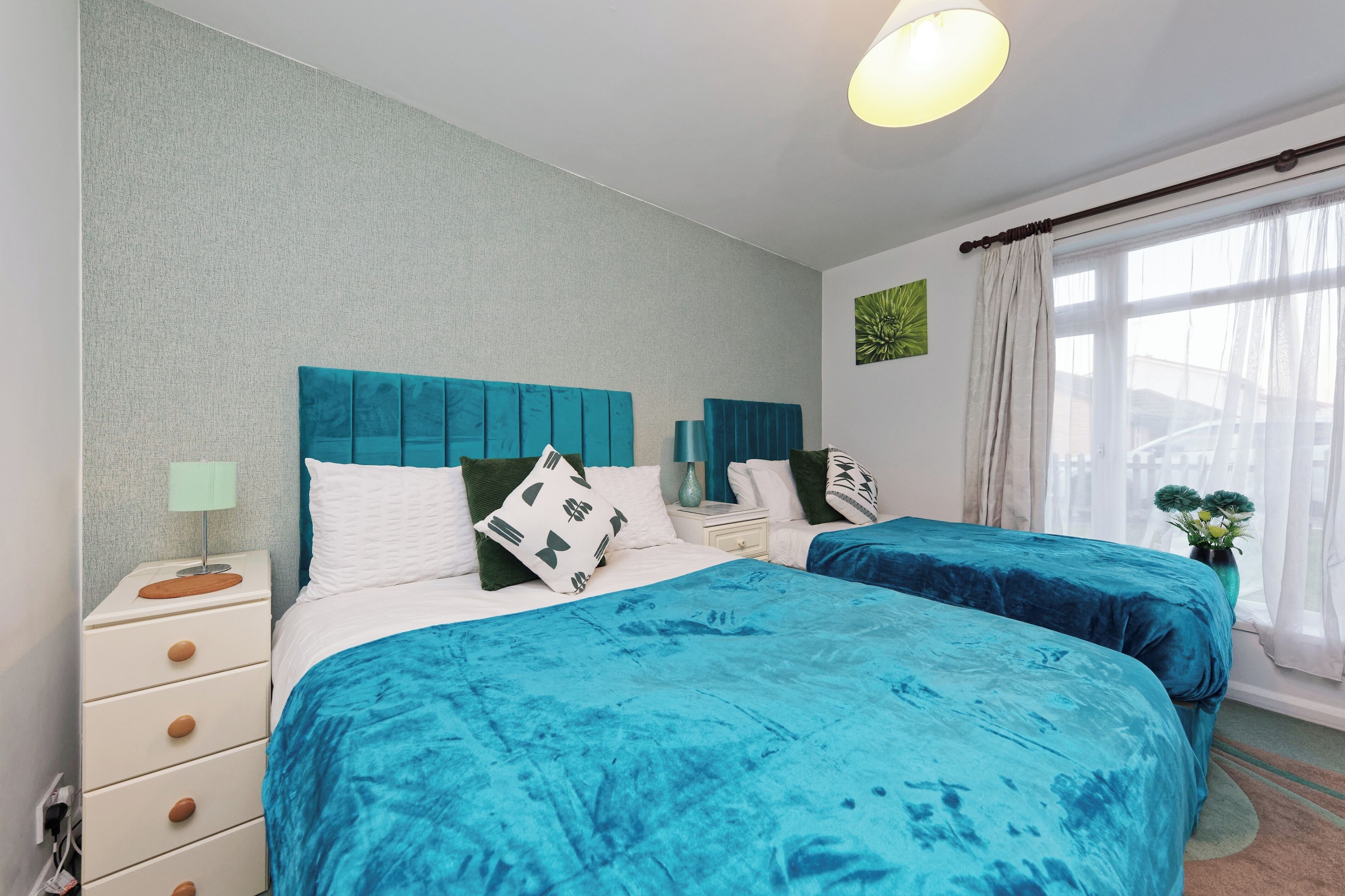 A bedroom with two beds, a nightstand, a lamp, and a window with curtains.