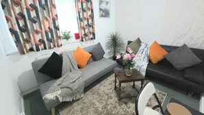 Ein Wohnzimmer mit einer Couch, einem Couchtisch, einem Sessel und einem Fenster mit gemusterten Vorhängen.