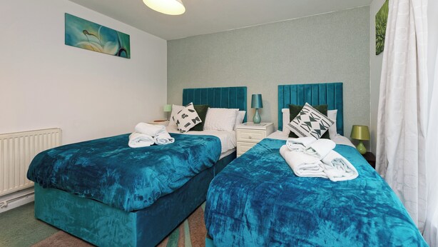 Ein Hotelzimmer mit zwei Betten, einem weißen Heizkörper, einem Bild an der Wand und einem Fenster mit Vorhängen.