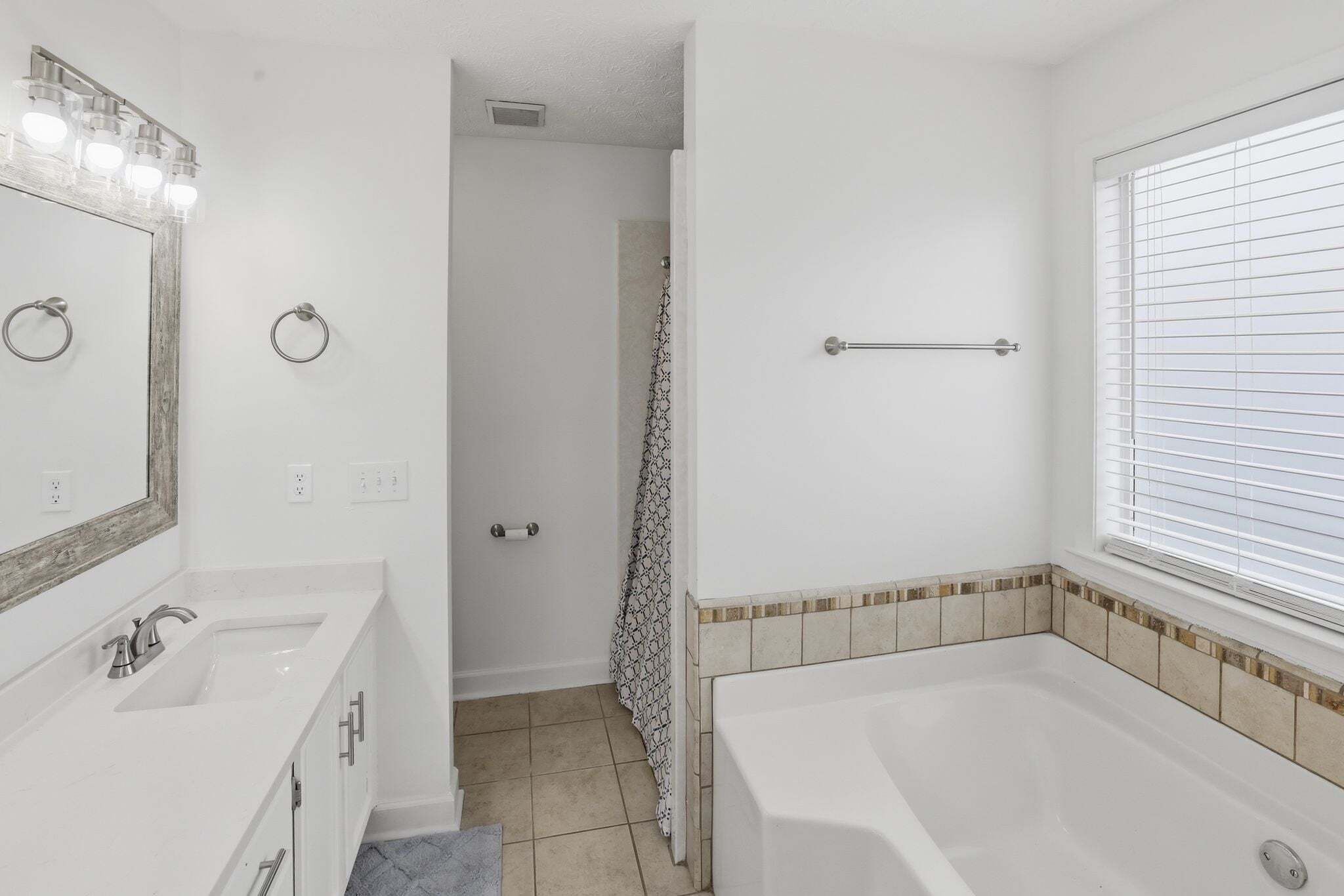 A bathroom with a bathtub, a vanity with a mirror, and a shower curtain.