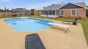 Ein Garten mit Schwimmbad, überdachter Terrasse und einem Ziegelhaus.