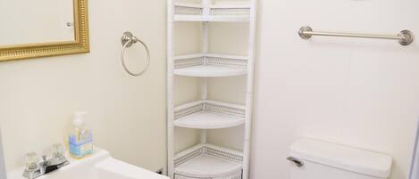 A bathroom with a white sink, a toilet, a wicker shelf unit, and a welcome sign.