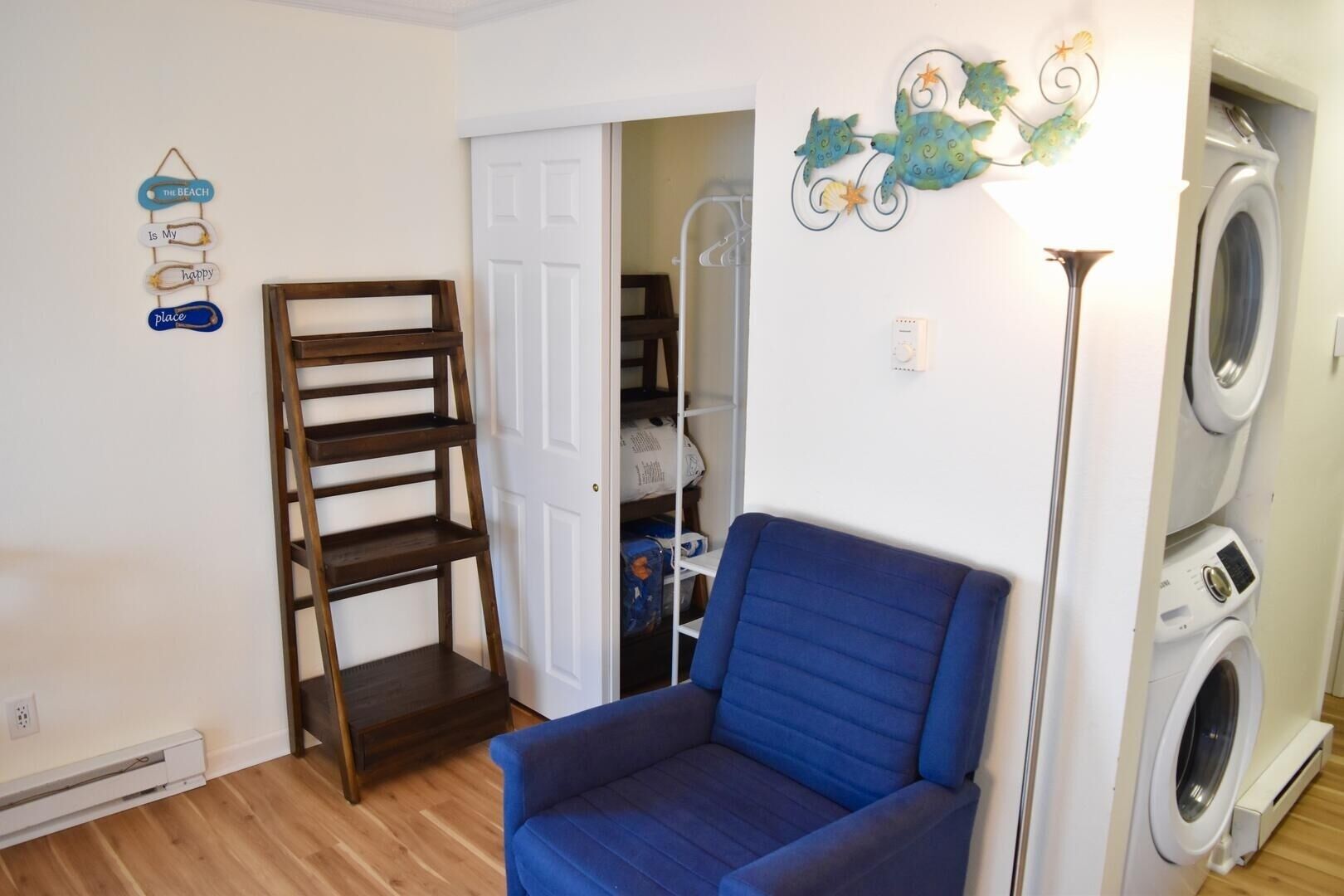 Una habitación con una silla azul, una escalera de madera, una puerta blanca, zona de lavandería y decoración mural.