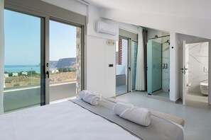 Habitación de hotel moderna con una cama grande, un balcón con vistas al mar, ducha de vidrio y baño independiente.