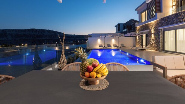 Ein Poolbereich mit Obstschale, Sitzgelegenheit im Freien und Blick auf ein Gebäude mit Steinverkleidung und großen Fenstern.