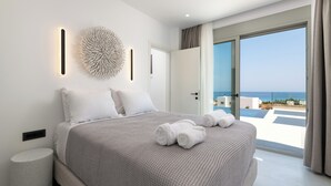 Ein modernes Schlafzimmer mit einem großen Bett, einer runden Wanddekoration und Meerblick durch eine offene Tür.