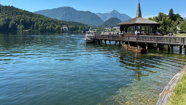Un muelle de madera se extiende hacia un lago, con un pabellón y un bote amarrado al final.