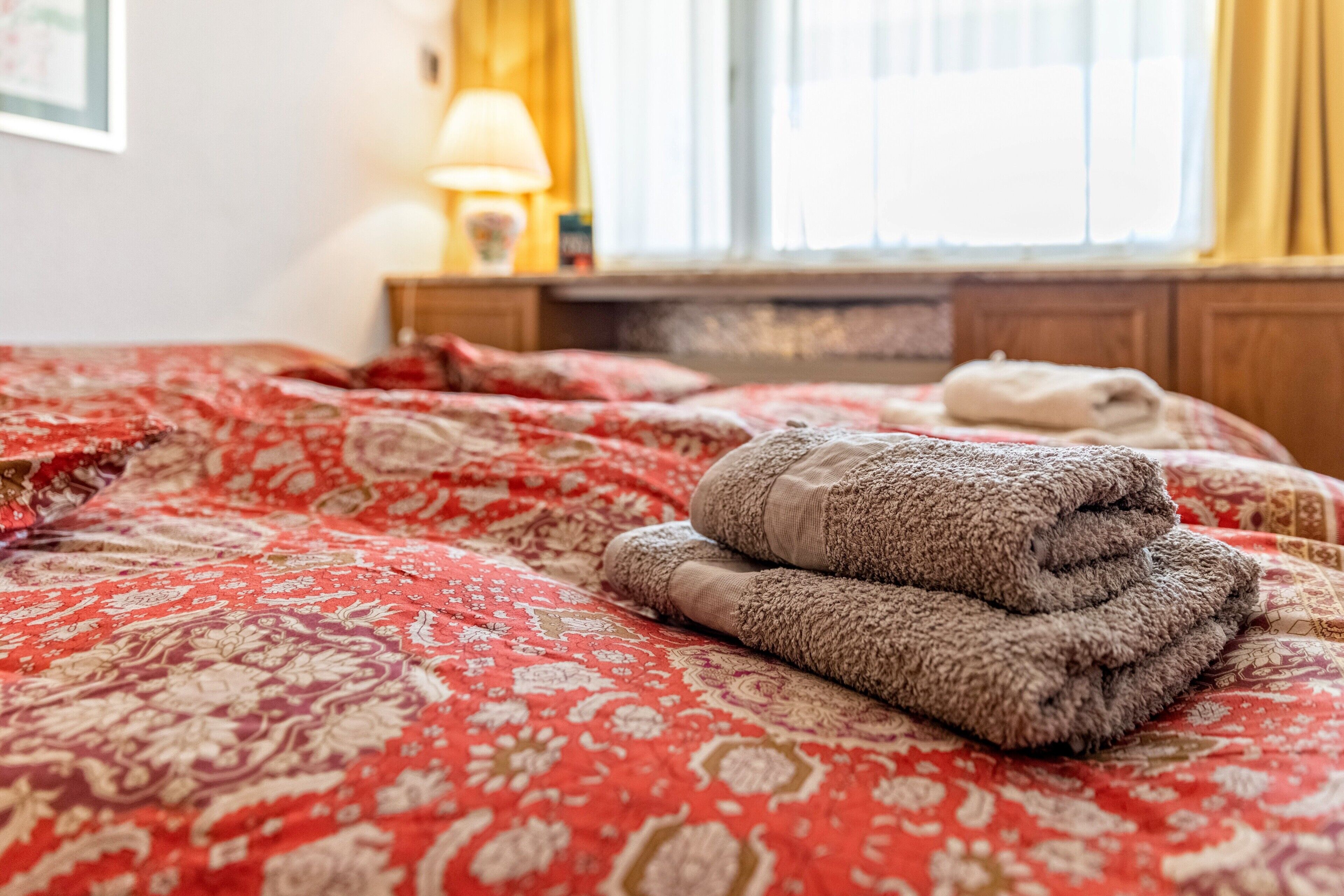 A neatly made bed with a patterned bedspread and folded towels.
