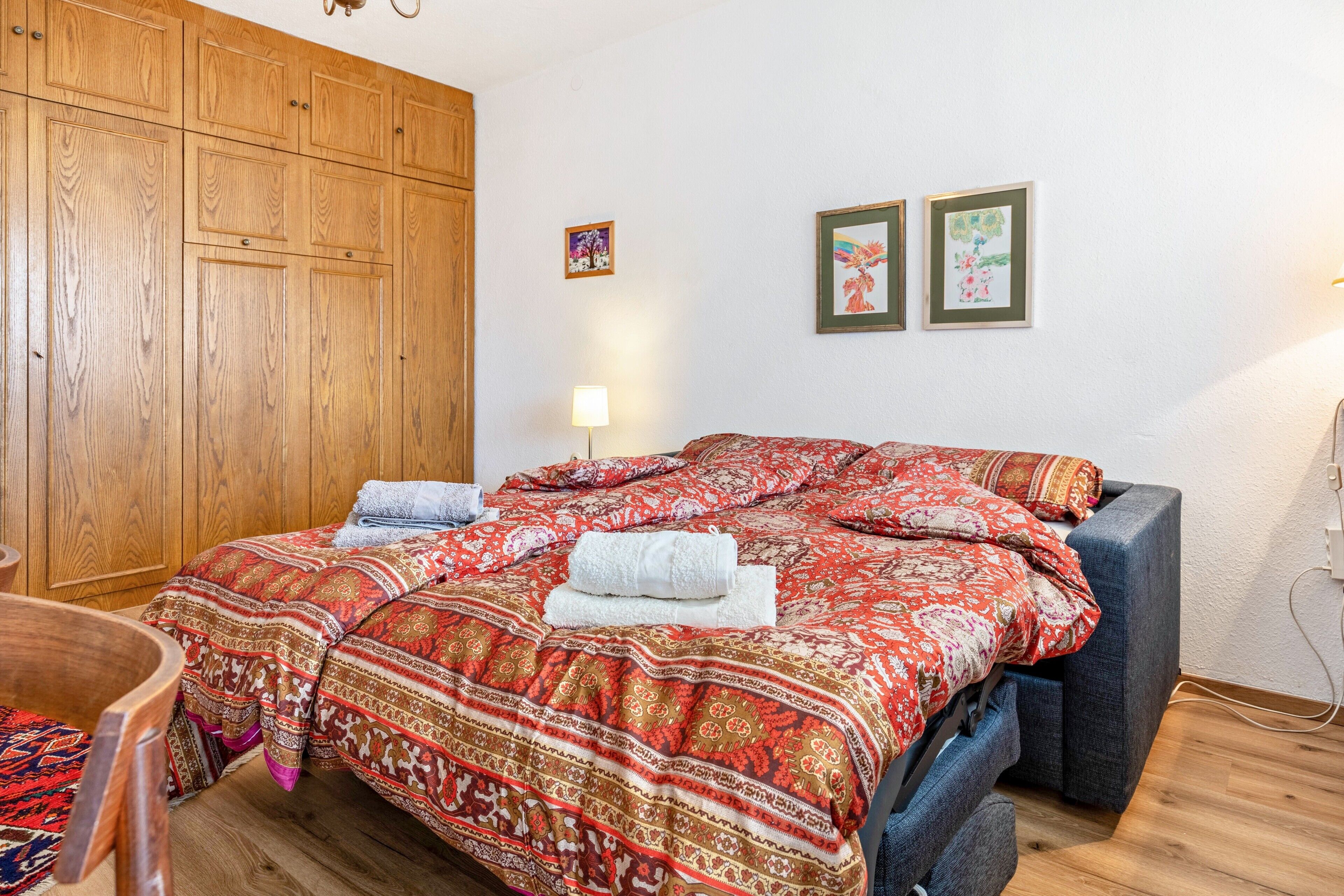 Une chambre avec une grande armoire en bois, un lit avec une literie à motifs et deux tableaux encadrés accrochés au mur.