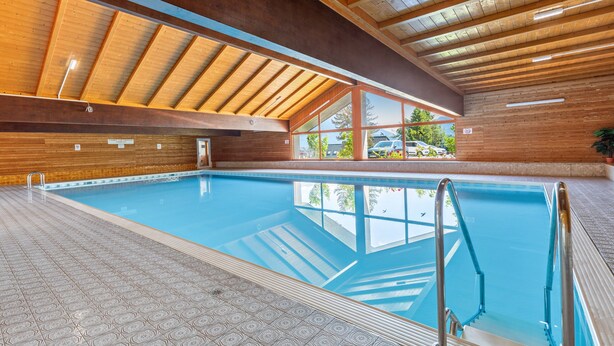 An indoor swimming pool with wooden beams, clear glass walls, and tiled flooring. - Grimmingblick Apartment with Pool and Spacious Terrace (Sonnenalm)