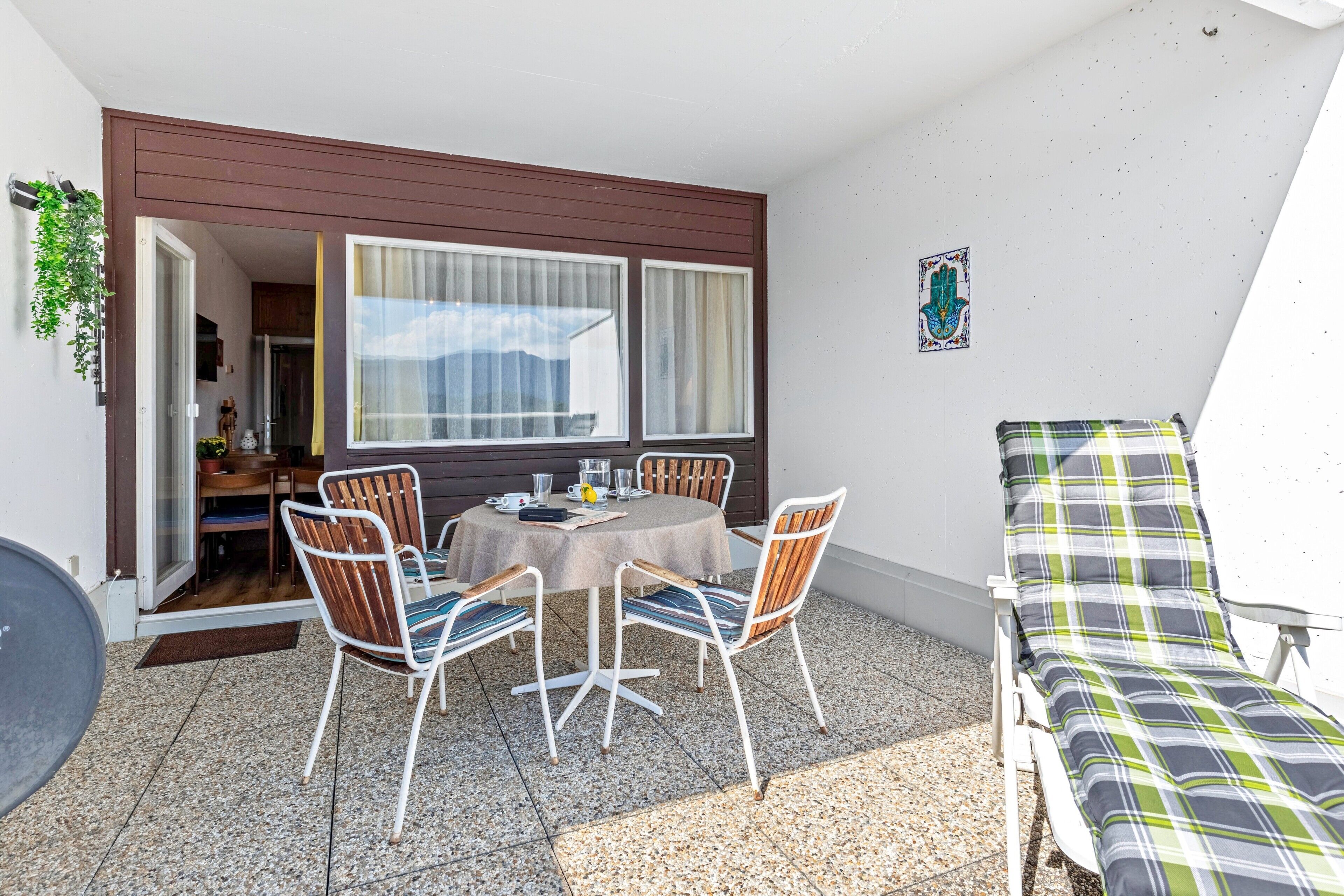 Um pátio com mesa e cadeiras, uma espreguiçadeira e uma porta que dá para o interior.