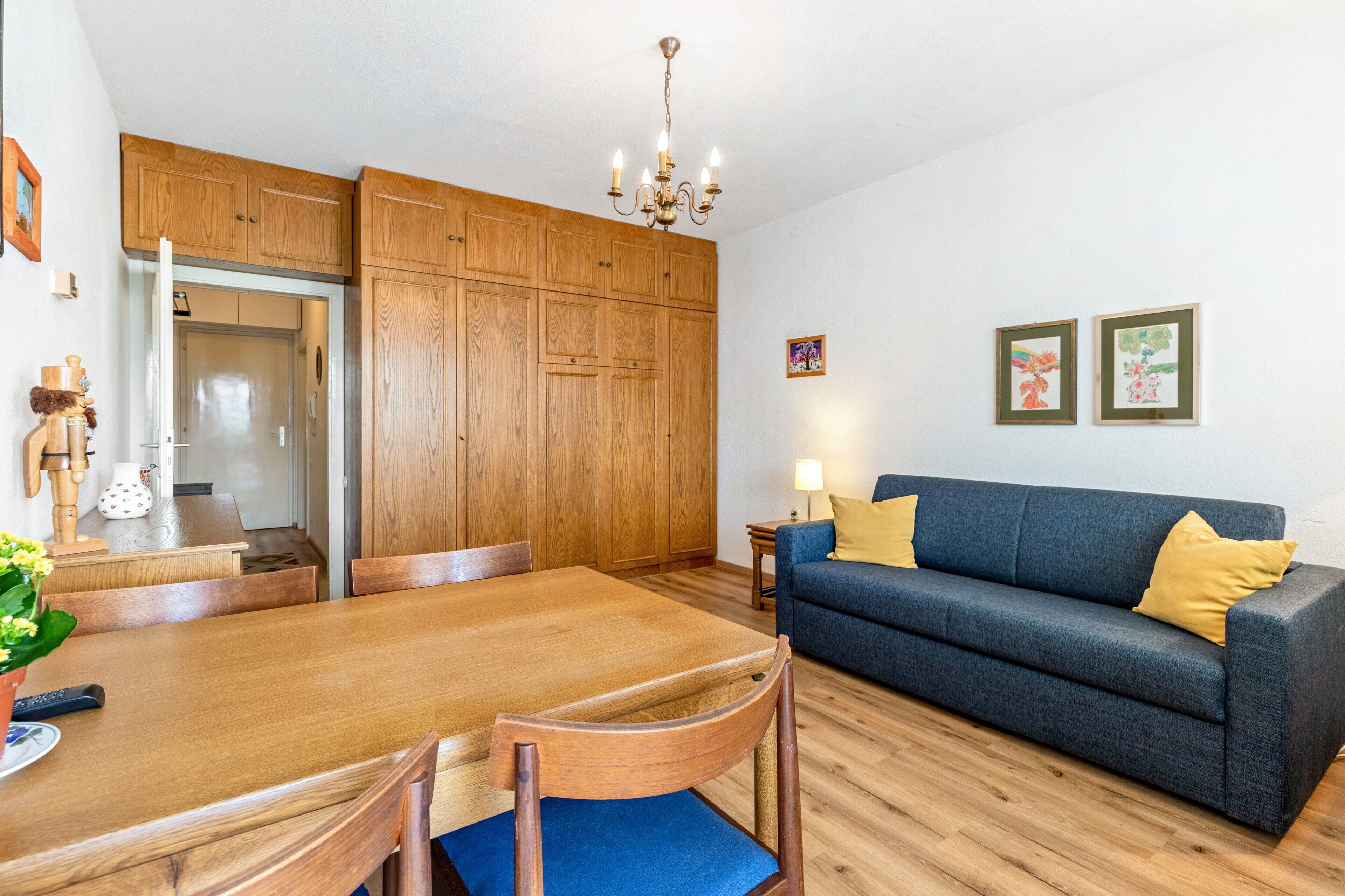 A dining area with a wooden table and chairs, a sofa, and a chandelier.