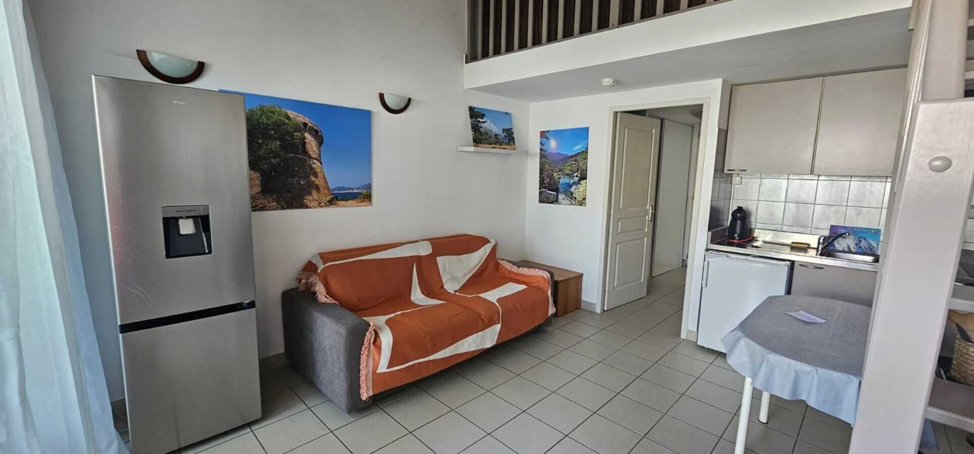 A compact living space with a kitchenette, a sofa, and a refrigerator.