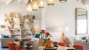 Ein moderner Essbereich mit einem zentralen Tisch, roten Stühlen, hängenden Pendelleuchten und einer Holzregaleinrichtung im Hintergrund.