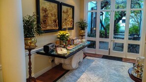A reception area with a marble floor, a reception desk, two framed artworks, and potted plants. - Tintagel Guest House (Cape Town)