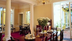 A dining area with a chandelier, a table set with silverware, and a vase of flowers. - Tintagel Guest House (Cape Town)