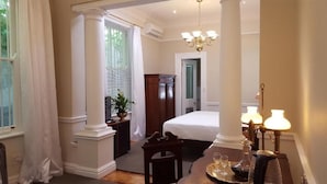 A bedroom with a bed, a nightstand, a desk with a lamp, and a window with curtains. - Tintagel Guest House (Cape Town)