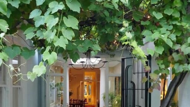 A patio with a table and chairs, surrounded by greenery and a view into a dining area. - Tintagel Guest House (Cape Town)