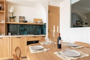 A modern kitchen with wooden cabinets, a green tiled backsplash, and a dining table set for four with wine glasses and a bottle. - Élégance & Confort au Cœur de Paris  (Paris)