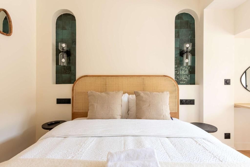A bed with a woven headboard, two bedside tables, and two wall-mounted sconces.