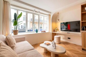 Ein modernes Wohnzimmer mit einer Couch, einem Couchtisch, einem Fernseher und einem großen Fenster mit Blick auf Gebäude.