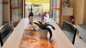 Ein Essbereich mit Tisch, Stühlen, einer Topfpflanze und Blick auf einen Garten durch offene Türen.