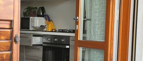 Una cocina con armarios, microondas, estufa y una ventana con cortinas.