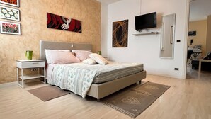 Ein Schlafzimmer mit Bett, Nachttisch, Lampe, Kunstwerk, Fernseher und einer Tür zu einem anderen Raum.