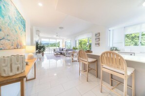 A spacious living area with a sofa, chairs, a dining table, and a kitchen counter. - Nalani On Airlie (Airlie Beach)