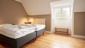 Een slaapkamer met een bed, een bankje, een nachtkastje en een raam.