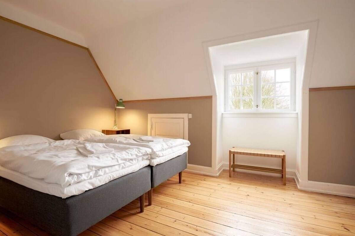 Une chambre à coucher avec un lit, une banquette, une table de chevet et une fenêtre.