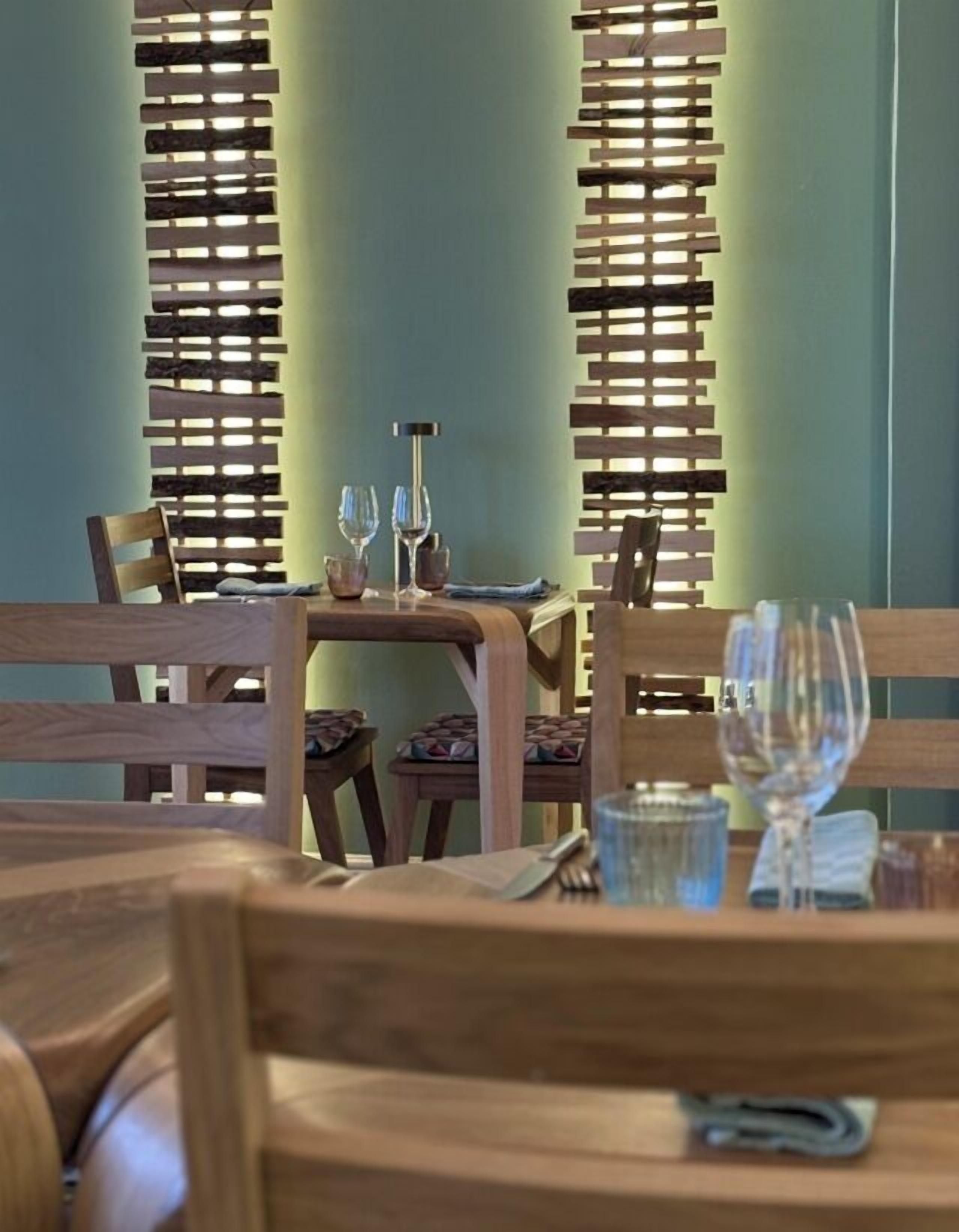 A dining area with wooden furniture, a table set with glasses and cutlery, and a vertical wooden partition with slats.