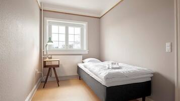Une chambre à coucher avec un lit, une fenêtre, un bureau avec une lampe et un radiateur.