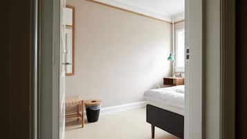 Un dormitorio con cama, mesita de noche, lámpara, cubo de basura y un banco de madera.