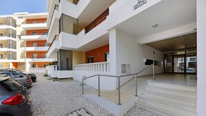 Un edificio a più piani con facciata bianca, ingresso coperto e un'area di parcheggio con auto.