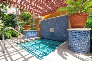 Une piscine aux carreaux de mosaïque bleus, une échelle en métal et des plantes en pot.