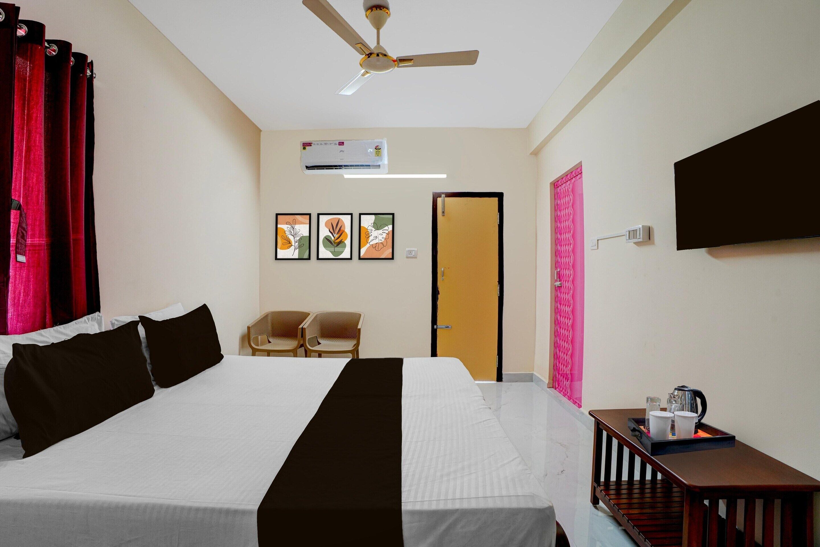 A hotel room with a bed, a ceiling fan, an air conditioning unit, a television, and a small table with a tray.