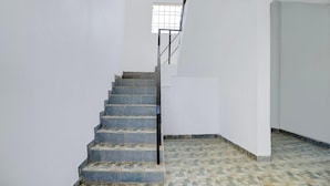 Una escalera de piedra con escalones que conducen a un rellano, paredes blancas y piso de baldosas.